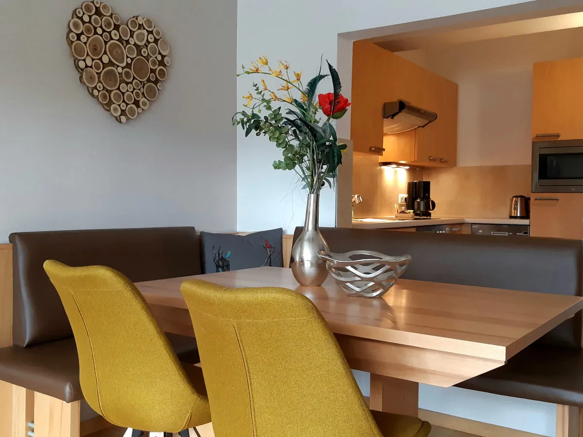 Essbereich mit Tisch, Stühlen und Blumenarrangement, Küche im Hintergrund