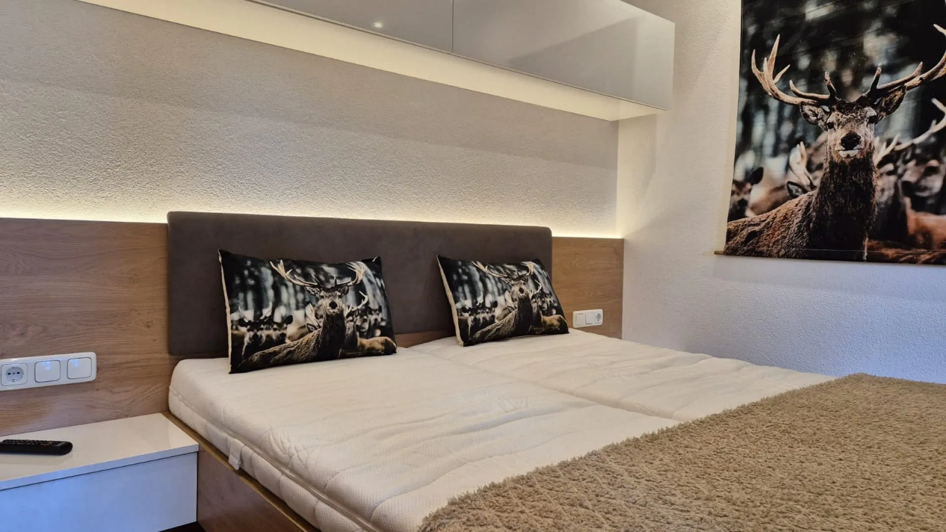 Schlafzimmer mit Doppelbett, dekorativen Kissen und Wandbild eines Rehs.